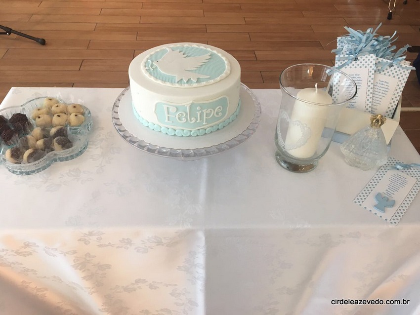 Mesa da comemoração do batizado com docinhos, bolo, vela e lembrancinhas